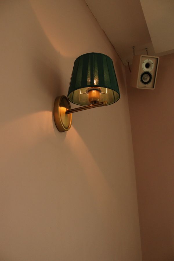 A lit wall sconce with a brass arm and green shade